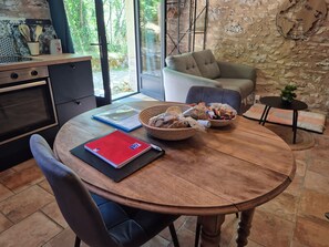 A dining area with a round wooden table, a red notebook, a blue folder, and a basket of snacks. - Gite Le Soupadou – La Framie – Charm, Comfort and Nature in Albas (Albas)