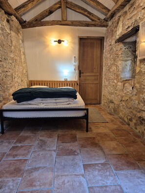 A bedroom with a bed, a wooden headboard, a stone wall, a wooden door, and a light fixture.
