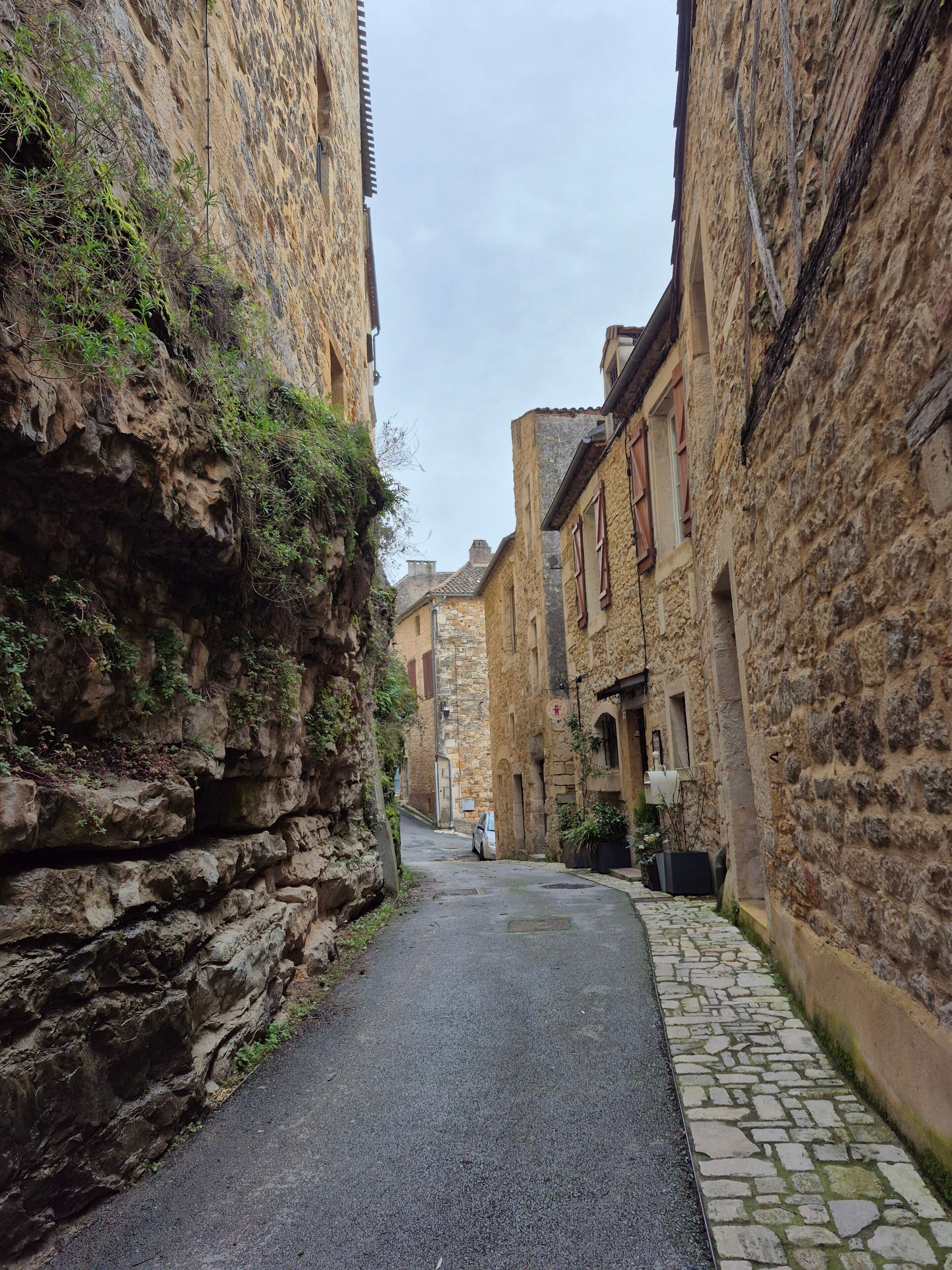 Une ruelle étroite, bordée de bâtiments en pierre, avec un chemin pavé et une voiture garée.