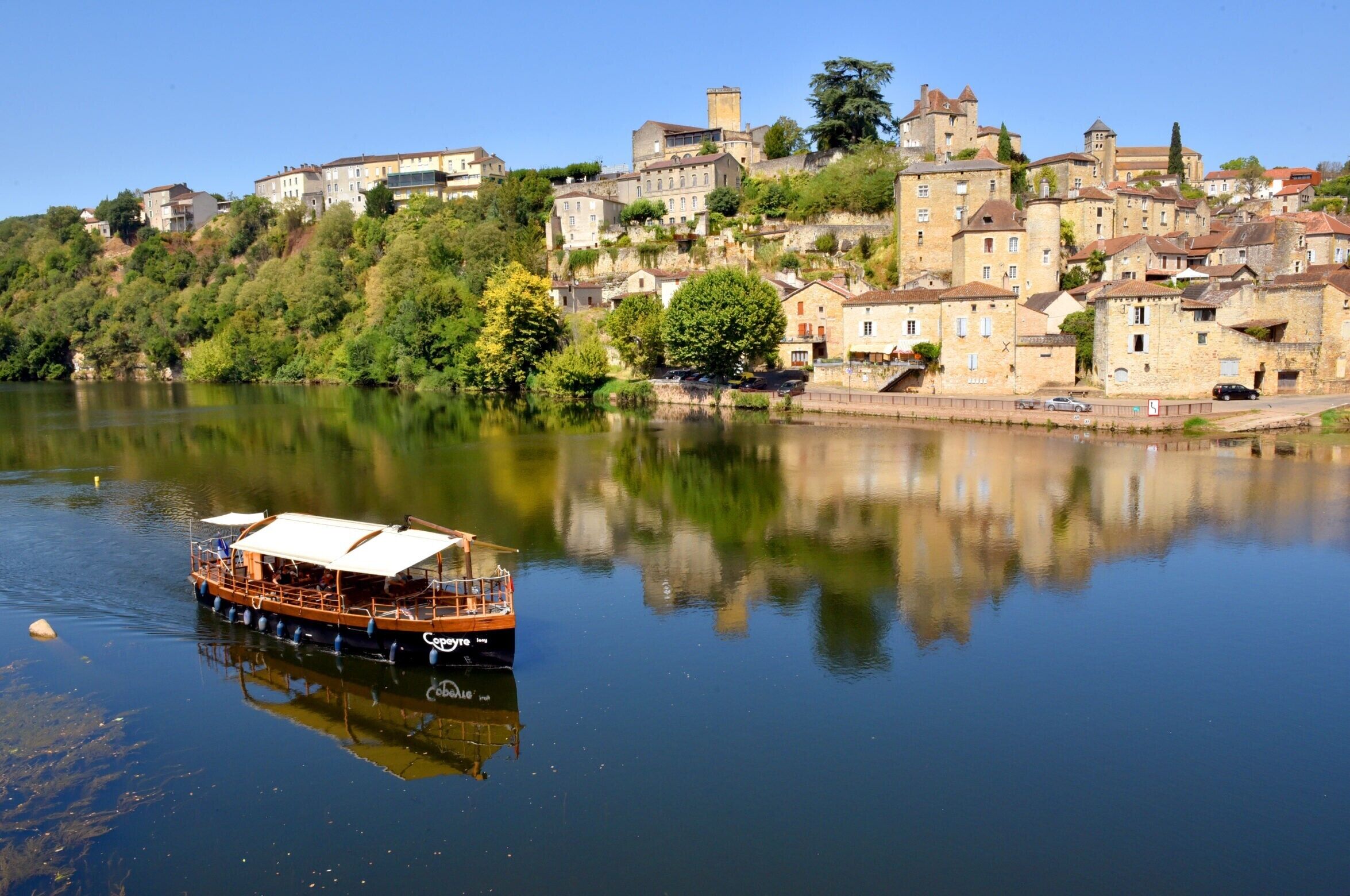Une rivière avec un bateau, des bâtiments sur une colline et un ciel dégagé.