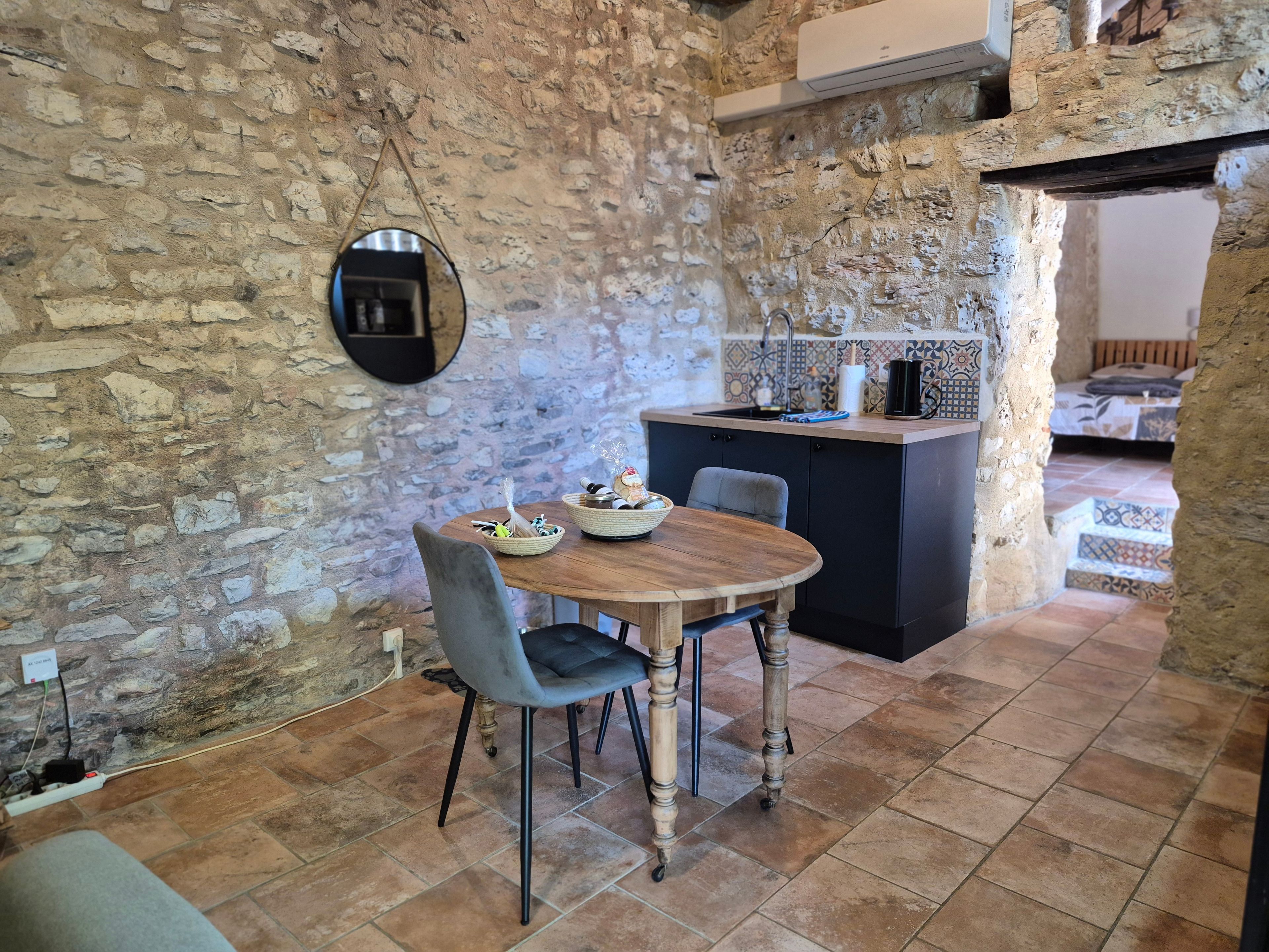 A rustic kitchen with a stone wall, a round wooden table, and a small island with a sink.