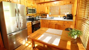 A kitchen with wooden cabinets, a stainless steel refrigerator, an oven, and a dining table with papers.