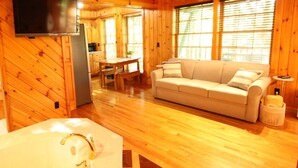 A wooden cabin interior with a sofa, a dining table, a TV, and a bathtub.