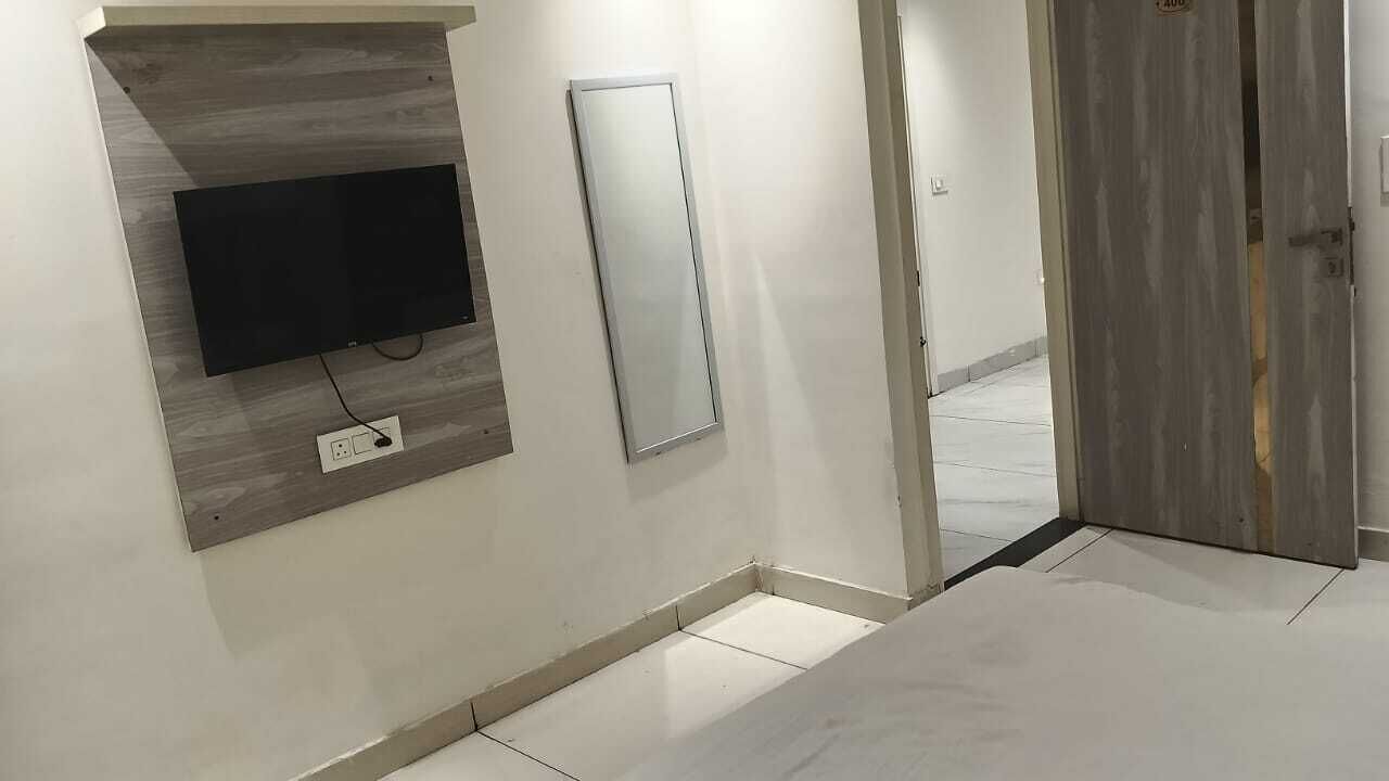 A room with a mounted TV, a mirror, and a door leading to another area.