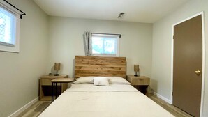A bedroom with a wooden headboard, a large bed, two bedside tables, a window, and a door. - Amazing 2-bedroom house with AC in Eastlake (Eastlake)
