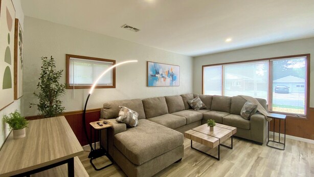 A modern living room with a sectional sofa, a coffee table, a small table with a plant, and a floor lamp. - Amazing 2-bedroom house with AC in Eastlake (Eastlake)