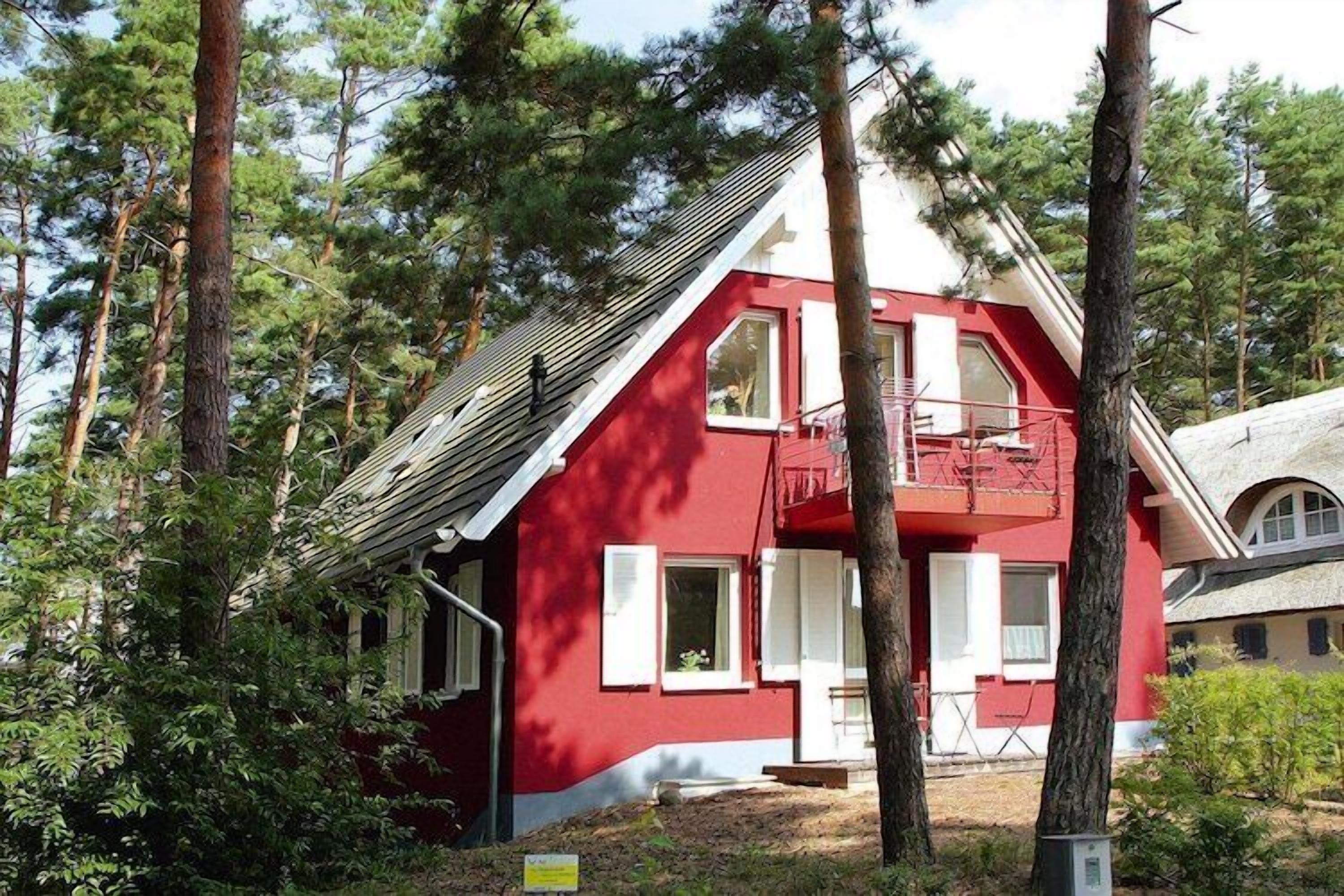 A red house with a balcony, surrounded by trees.