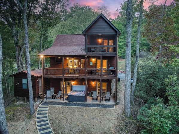 A two-story log cabin with a balcony, a hot tub, and a deck with outdoor seating.
