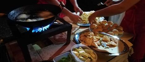 A cooking scene with a wok on a portable stove, various food items on a table, and containers of vegetables.