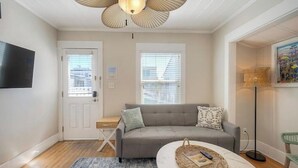A living room with a grey sofa, a round coffee table, a ceiling fan, and a TV mounted on the wall. - 4BR Beach Bungalow - Great for multiple families! (San Diego)