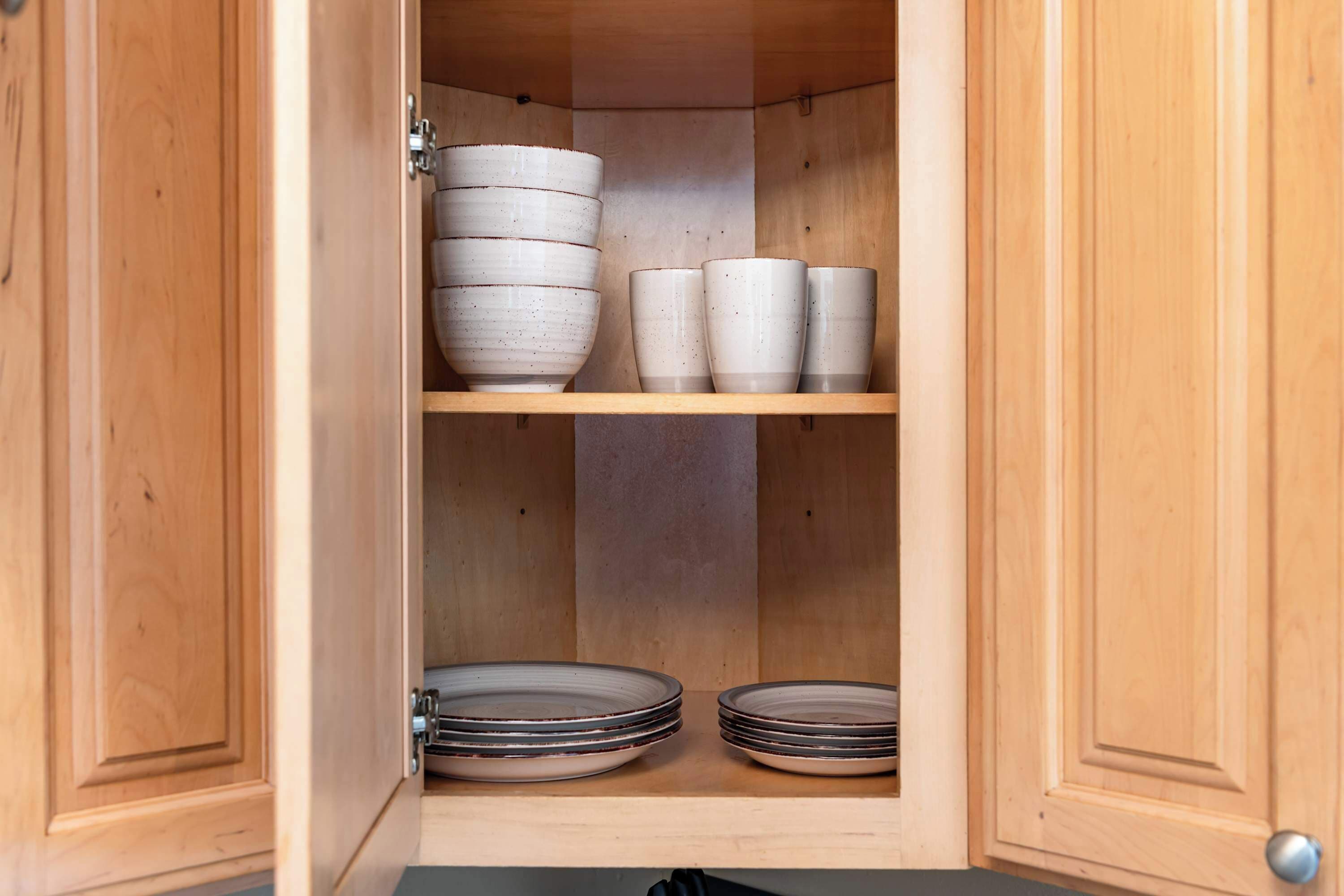 A wooden cabinet with shelves holding white ceramic bowls, cups, and plates.