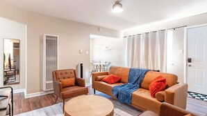 Ein Wohnzimmer mit braunem Ledersofa, einem runden Holztisch, einem braunen Sessel und einer weißen Deckenleuchte.