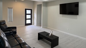 Un salon moderne avec un canapé en cuir, une table basse noire, un ventilateur de plafond et un téléviseur fixé au mur.