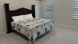 Une chambre à coucher avec un grand lit, une tête de lit en bois et deux fenêtres équipées de stores.