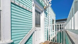 A narrow wooden deck leading to a turquoise building with a white door and a small window.