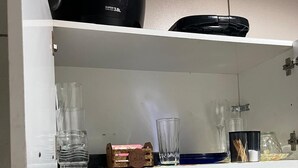 Uma área de cozinha com cafeteira, copos e um cardápio na parede.