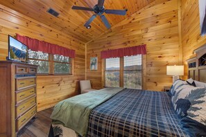 Ein Schlafzimmer einer Holzhütte mit einem Bett, einem Schminktisch und einem Deckenventilator.