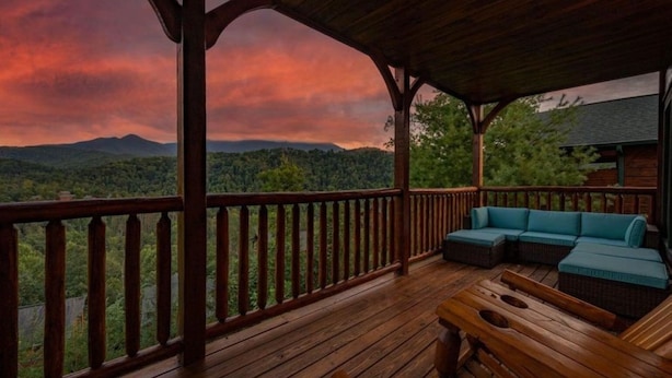 Une terrasse en bois avec un canapé bleu et une table en bois, offrant une vue sur un paysage boisé avec des montagnes à l’horizon.