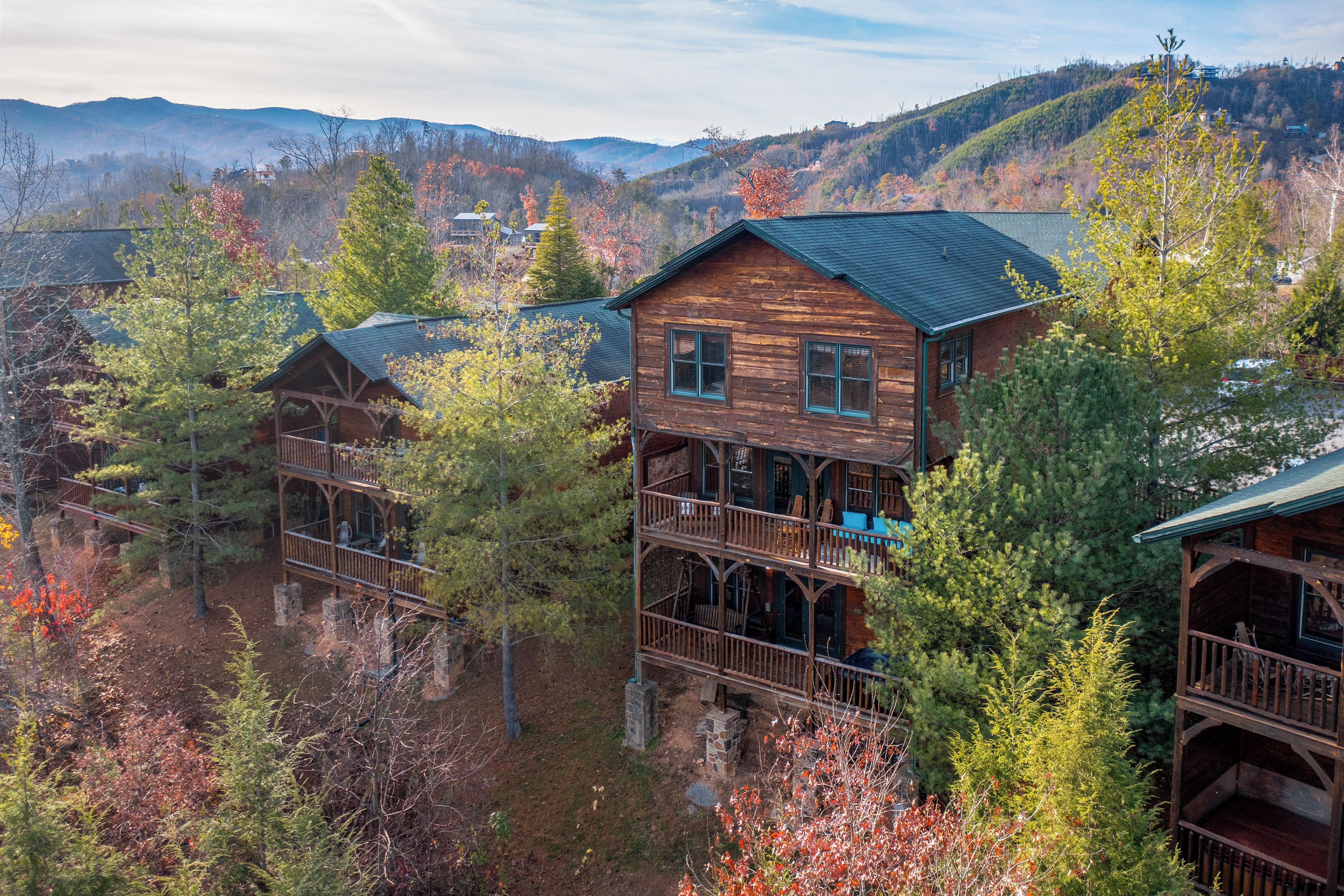 Ein mehrstöckiges Blockhaus mit Balkon, umgeben von Bäumen und einer Berglandschaft im Hintergrund.