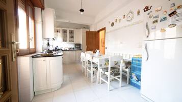 Una cocina con armarios blancos, una mesa de comedor con sillas y un refrigerador.