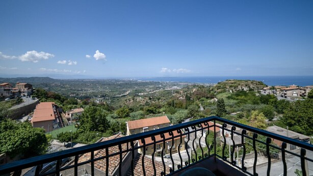A balcony with a view of a coastal town, buildings, and greenery. - Il rifugio del templare  - Appartamento Cavaliere (Roccavaldina)