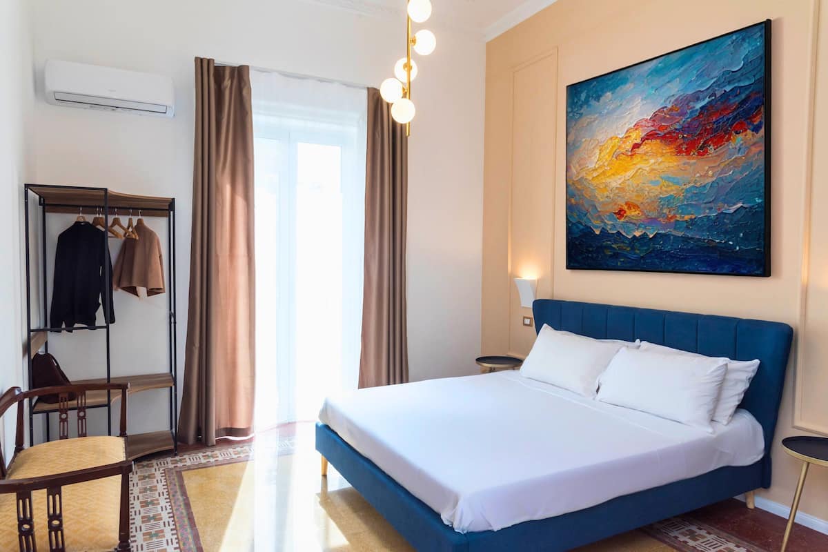 A hotel room with a large bed, a wardrobe, a desk, and a painting on the wall.