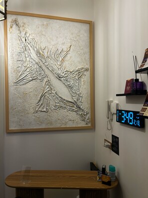 A room with a large abstract painting, a wooden table, a digital clock, and a Wi-Fi sign.