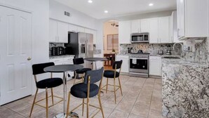 Una cocina moderna con armarios blancos, encimera de granito y comedor con mesa y sillas.