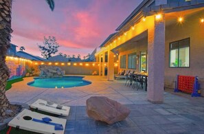 Un área de piscina con sillones de descanso y un jacuzzi, rodeada por un porche cubierto con guirnaldas de luces.