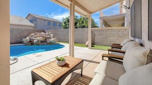 Un espacio exterior cubierto con piscina, una mesa de madera y un sofá blanco.