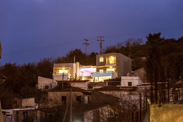 Un bâtiment moderne doté de nombreuses fenêtres illuminées, entouré d’arbres et d’autres constructions.