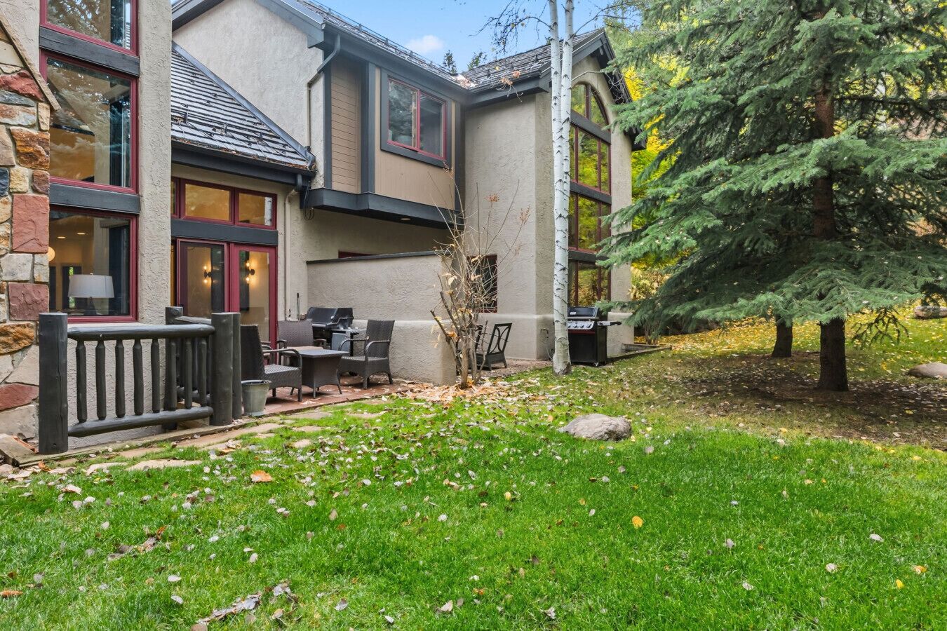 A modern house with a stone exterior, a patio with outdoor furniture, and a large tree in the yard.
