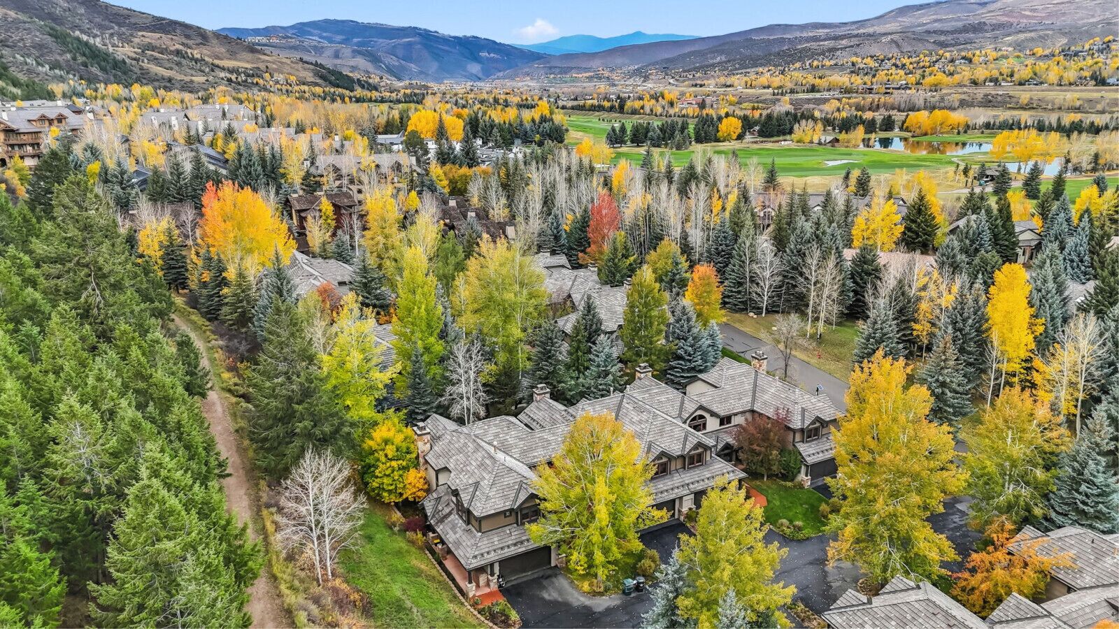 A residential area with houses surrounded by dense forests and a golf course in the background.