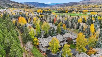 A residential area with houses surrounded by dense forests and a golf course in the background.