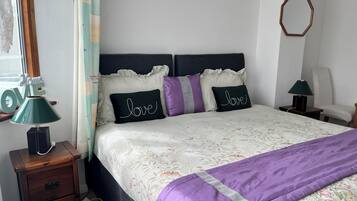 A neatly made bed with floral bedding, a purple throw blanket, and decorative pillows with the word 'love.'