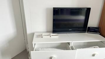 A white desk with a flat-screen TV, two drawers, and a small shelf with two boxes labeled 'love' and 'home.'
