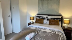 Un dormitorio ordenado con cama, dos lámparas de noche, un cuadro y una puerta.