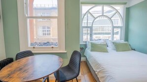 Huoneessa on sänky, pöytä ja kaksi tuolia. Siinä on kaksi suurta ikkunaa, joiden yläosa on kaareva.