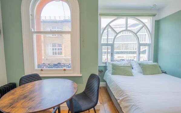 Una habitación con cama, una mesa y dos sillas. Cuenta con dos ventanas amplias con arcos.