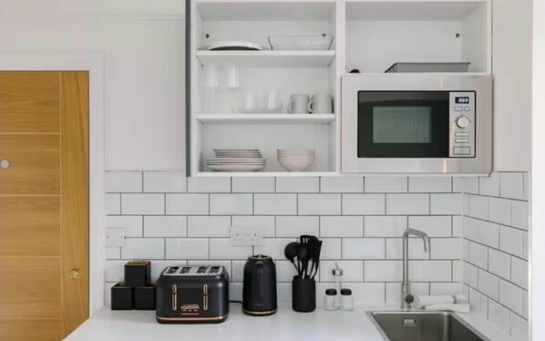 A kitchen with white cabinets, a microwave, a toaster, and a sink.
