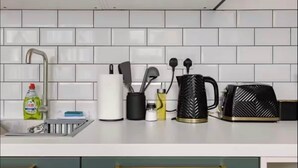 A kitchen with white tiled backsplash, a stainless steel sink, and various kitchen utensils and appliances. - Modern King's Cross Studio 004 (London)