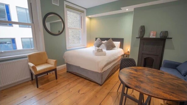 A bedroom with a bed, a chair, a table, a fireplace, and a window. - Modern King's Cross Studio 004 (London)