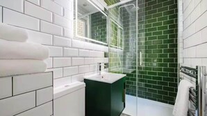 A modern bathroom with white and green tiles, a black sink, and a glass shower enclosure. - Modern King's Cross Studio 004 (London)