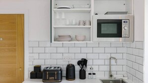 Eine moderne Küche mit weißen Fliesen, einer eingebauten Mikrowelle, einem Toaster und einem Spülbecken.