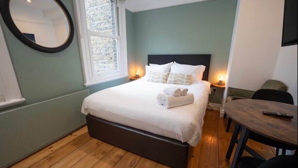 Ein Schlafzimmer mit Bett, Nachttischlampen, einem runden Spiegel, einem Fenster und Holzboden.