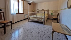 Une chambre à coucher avec un lit en bois, une chaise, une table de chevet avec une lampe et une fenêtre avec des rideaux.