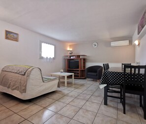 Una sala de estar pequeña y amoblada con sofá, mueble para televisión, mesa de comedor con sillas y un reloj en la pared.