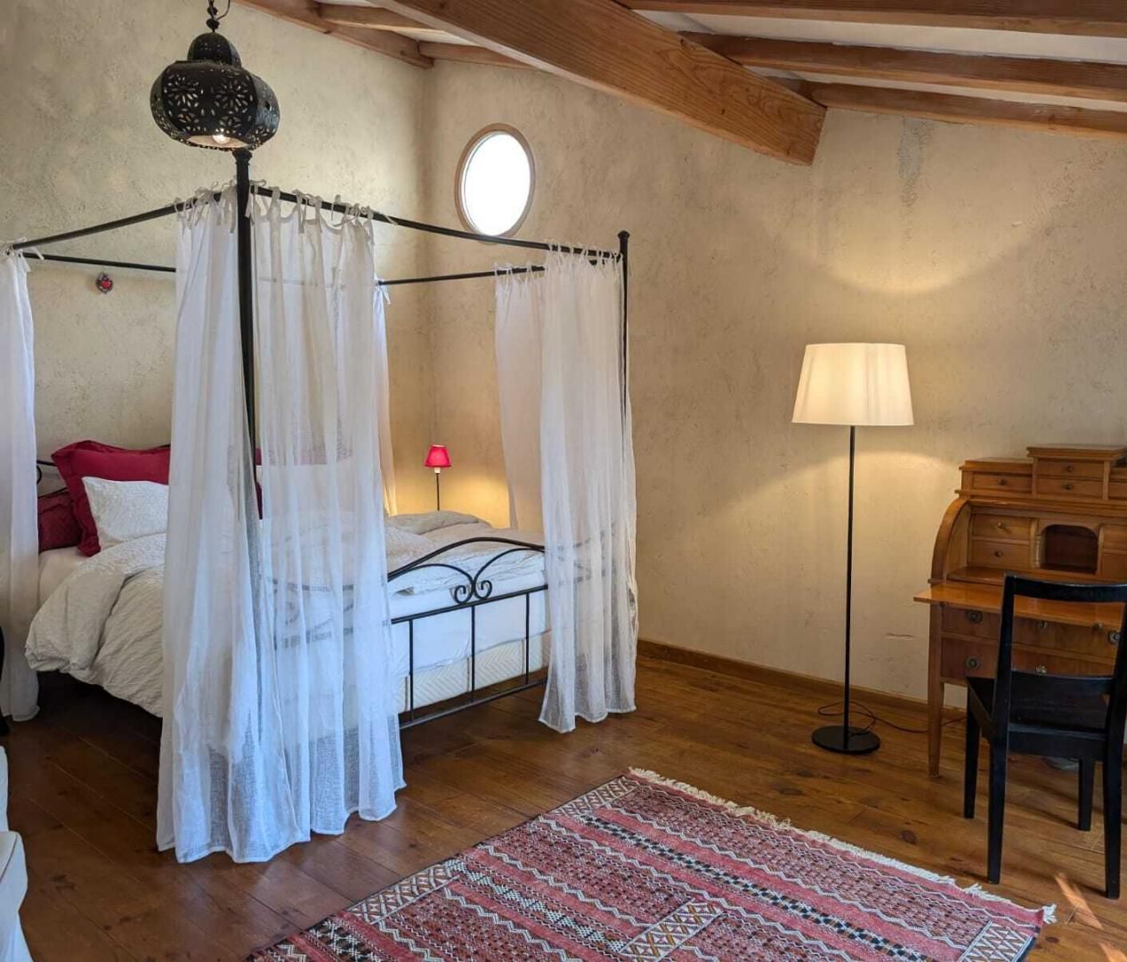 Une chambre à coucher avec un lit à baldaquin, un bureau avec une chaise, une lampe sur pied et un tapis à motifs.