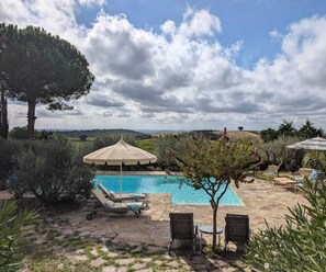 A pool area with lounge chairs, umbrellas, and a view of the countryside.