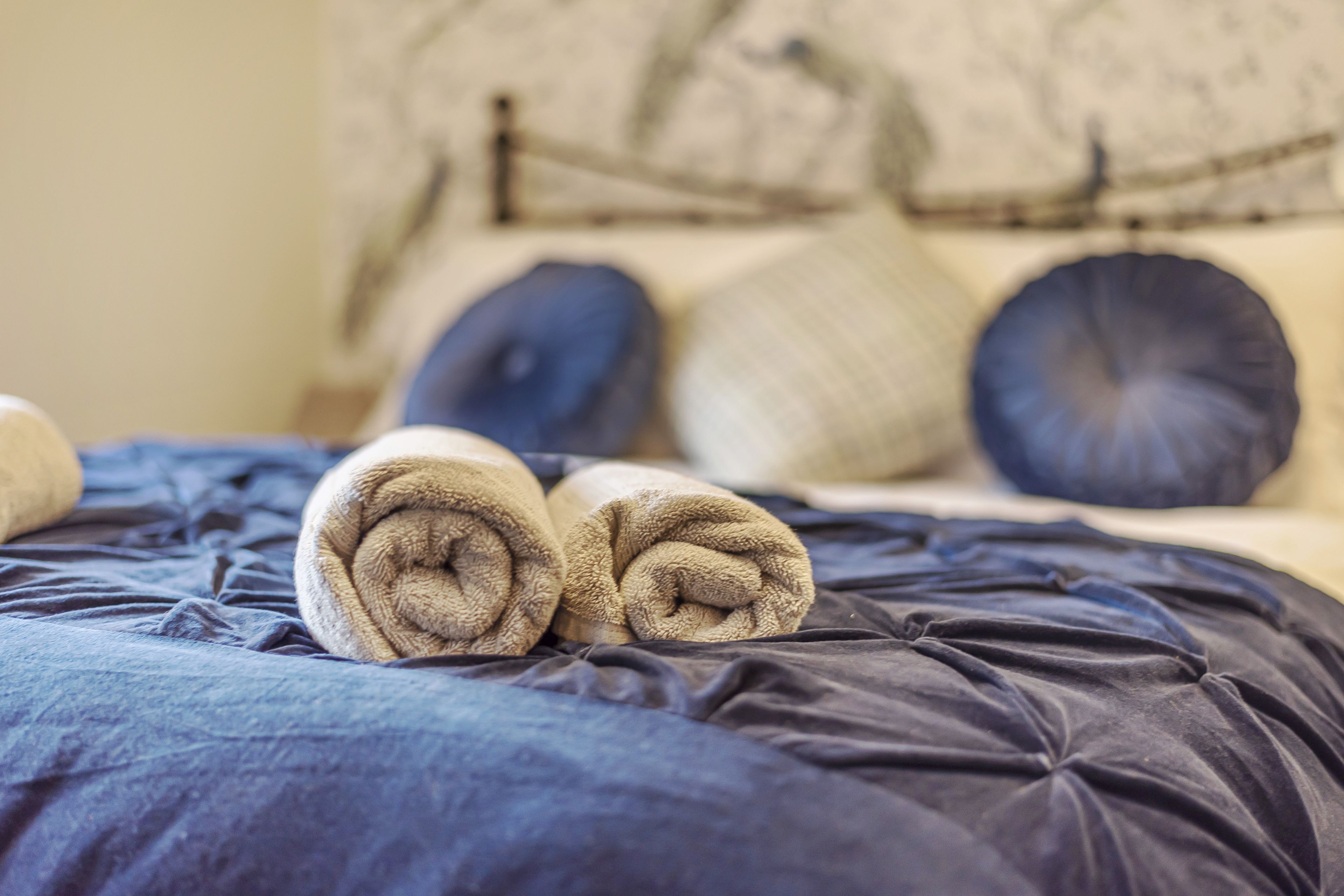 A bed with rolled towels and a dark blue comforter.
